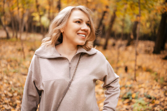 Smiling woman on autumn walk looking away &mdash; pure happiness and relaxation. Mental health care and mindfulness practice. Joyous lady enjoying seasonal foliage feeling positive mood in yellow woods.