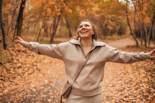Joyful woman traveler with outstretched arms in autumn forest. Happy hiker standing among yellow trees enjoying nature. Freedom concept for nature lover outdoors.
