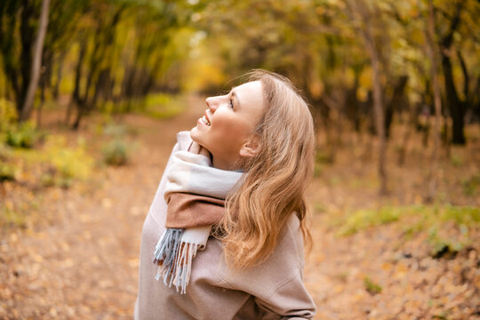 Smiling woman traveler profile in plaid scarf in autumn forest. Joyful blogger looking up among yellow trees. Concept of enjoying weather outdoors.