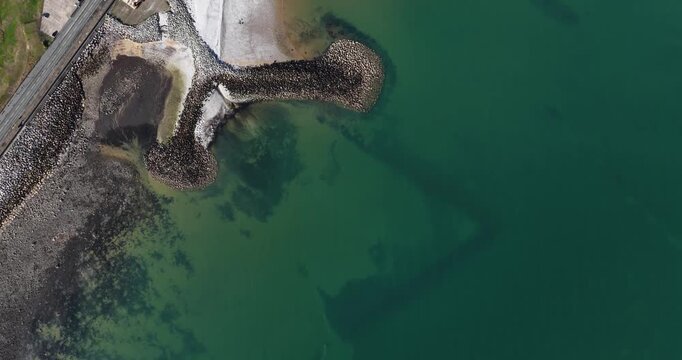 Aerial footage looking directly down over Penrhyn Bay North Wales showing the curved beach clear coastal water rocky breakwaters shoreline road and nearby parking area from a high drone view