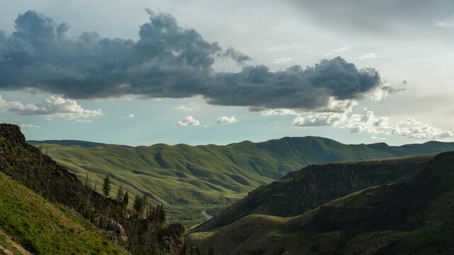 View of rolling green hills and dramatic clouds over a mountainous landscape in Idaho, United States.