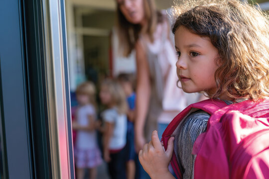 The image captures a girl with a bright pink backpack standing at the school entrance, highlighting her curiosity and readiness to start a new adventure.