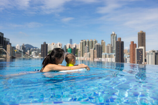 Mother holding toddler boy in rooftop pool overlooking hong kong city