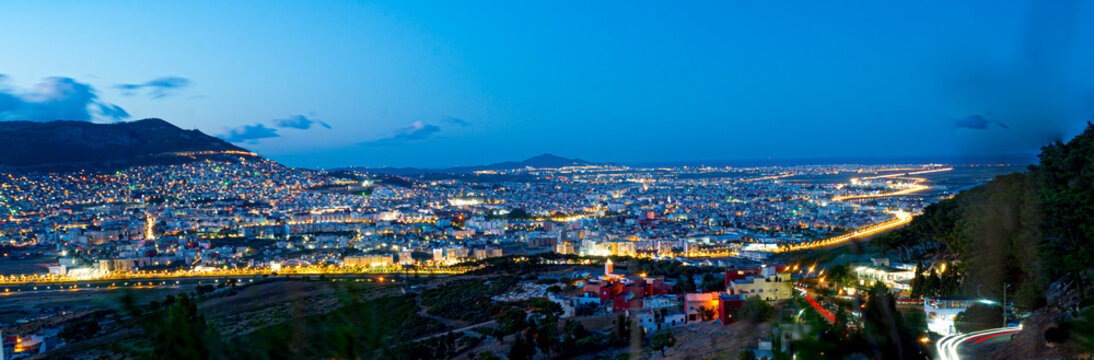 Tetouan cityscape at dusk from Jbel Bouanan, featuring the city lights, Jbel Dersa in the background, along with Martil town enlighted road leading up to it and Cabo negro by the Mediteranian sea