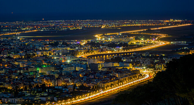 City of Tetouan close-up cityscape view at night from Jbel Bouanan Mount, featuring the enlighted road leading up to Martil beach town passing Sania Rmel airport and Mediterranea sea in the background