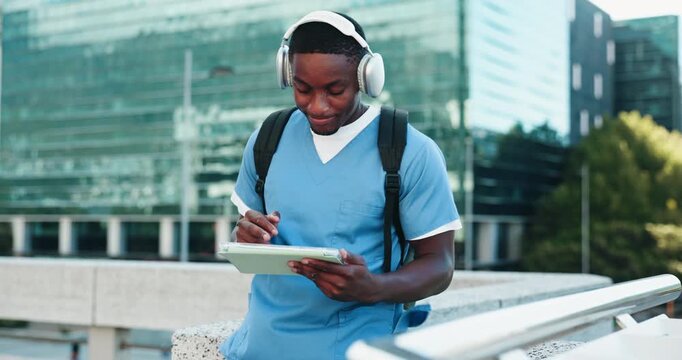 Headphones, doctor and student with tablet in city studying for clinical exam or test. Education, technology and African male healthcare intern listening to music and reading online textbook in town
