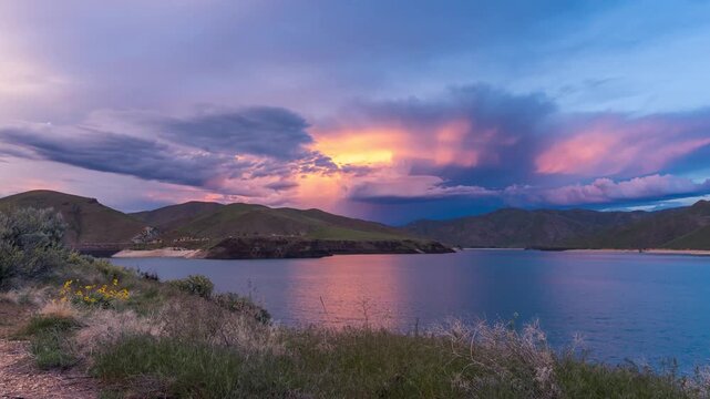 View of Lucky Peak Lake at sunset with dramatic clouds over the surrounding hills and calm water in Ada County, Idaho, United States.