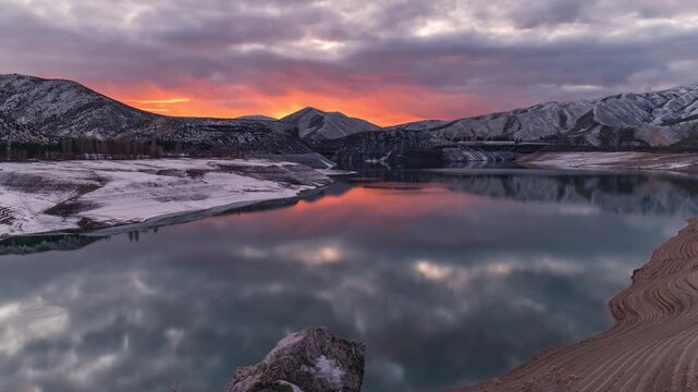 View of Lucky Peak Lake at sunset with snow-dusted mountains and calm water reflecting the colorful sky in Ada County, Idaho, United States.