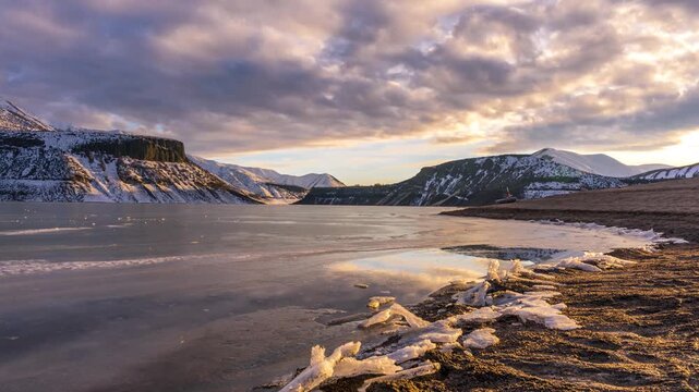 View of Lucky Peak Lake with frozen shore and snowy hills under a dramatic sunset sky in Ada County, Idaho, United States.