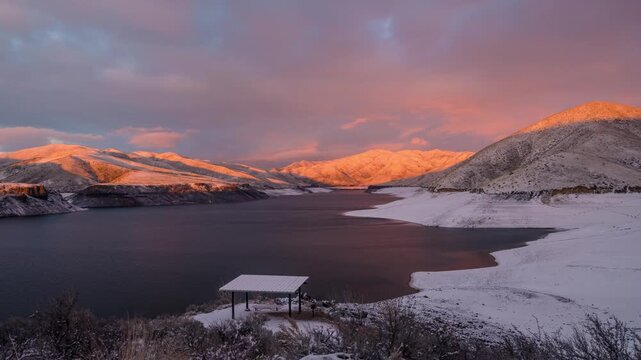 View of Lucky Peak Lake at sunset with snow-covered hills and a picnic shelter in Ada County, Idaho, United States.