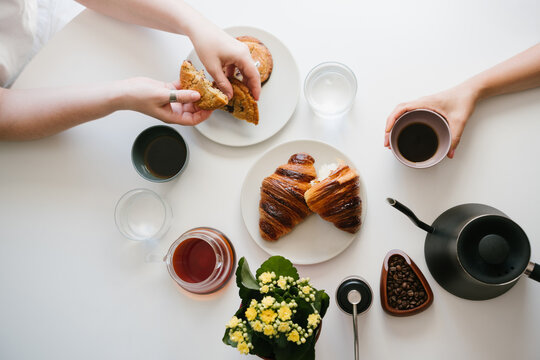 Two Friends Having Black Coffee and Sharing Chocolate Chip Cookies at a White Breakfast Table with Croissants, Water, Coffee Beans, Hand Grinder, Gooseneck Kettle and Yellow Flowers. top view