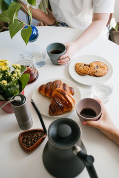 Morning Coffee for Two with Golden Croissants and Chocolate Cookies on a Bright Table with Hand Grinder, Coffee Beans, Kettle and Green Plants. vertical composition