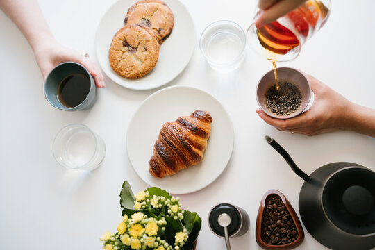 morning coffee. Two Friends Sharing Fresh Pour Over Coffee at a White Table with Croissant, Chocolate Chip Cookies, Water Glasses, Coffee Beans, Hand Grinder, Gooseneck Kettle and Yellow Flowers. top 