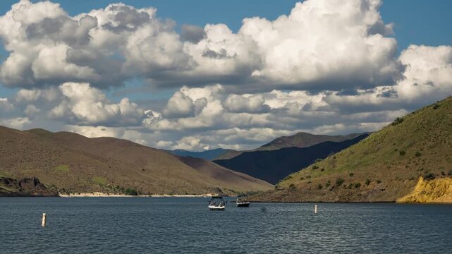 View of Lucky Peak Lake with rolling hills and a boat on the water under a cloudy blue sky in Ada County, Idaho, United States.