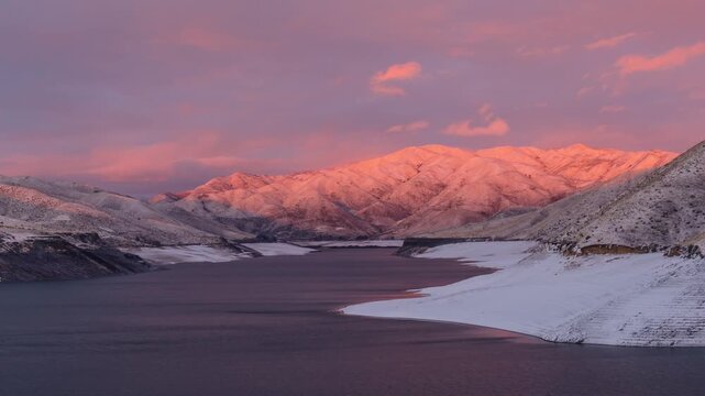 View of Lucky Peak Lake surrounded by snow-covered mountains during a golden sunset in Ada County, Idaho, United States.