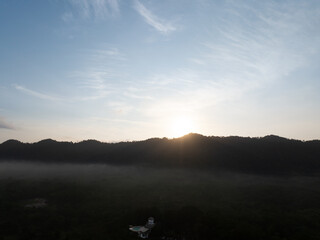 Sunrise over a misty tropical mountain forest with morning fog. Natural landscape with expansive sky for travel and environmental themes. Nature, tourism and conservation. Climate, ecology concepts. © Fahroni