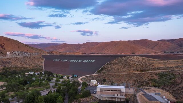 View of a dam featuring the message Keep Your Forests Green, surrounded by rolling hills and trees under a soft sunset sky in Idaho, United States.