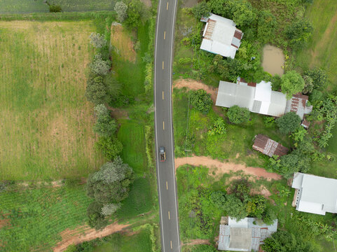 Drone view of paved country road between farmland and village homes during wet growing season, showing rural infrastructure that connects farming communities, agriculture and local food production.