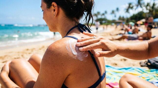 Applying sunscreen on a woman's shoulder at the beach on a sunny day