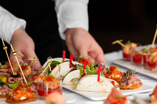 A waiter serves variety of gourmet catering appetizers and canapes on plates during a catered event.