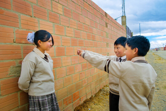 Two school-age children laughing at their classmate in her uniform in La Paz, Bolivia - concept of education
