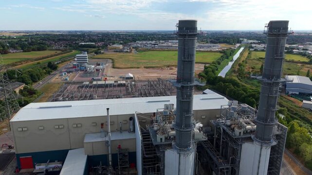 Close-up aerial view of gas-fired power station exhaust stack with high-voltage electrical substation in the background in Spalding, Lincolnshire, UK