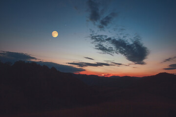 Full Moon, stars and planets above landscape silhouettes in blue hour time. © astrosystem