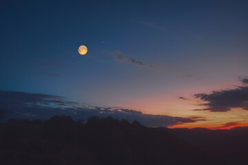 Full Moon, stars and planets above landscape silhouettes in blue hour time. © astrosystem
