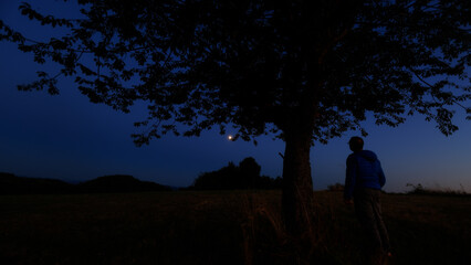 Silhouette of a person in nature observing night sky, Moon, stars and planets from a remote location. © astrosystem