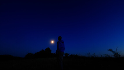Silhouette of a person in nature observing night sky, Moon, stars and planets from a remote location. © astrosystem