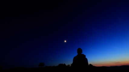 Silhouette of a person in nature observing night sky, Moon, stars and planets from a remote location. © astrosystem