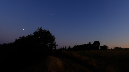Moon on a twilight sky with stars, planets and landscape mountain silhouettes. © astrosystem