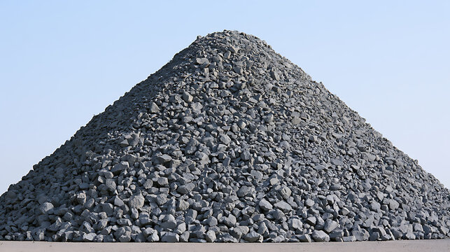 A massive pyramid-shaped pile of grey crushed stone and gravel aggregate under a clear blue sky, ready for construction and industrial use