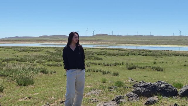 One Asian woman enjoying scenic landscape of salt lake wetland and distant wind turbines in summer in Ulan Hada Volcano Geopark, Ulanqab, Inner Mongolia, China