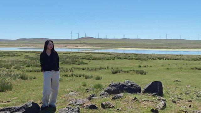 One Asian woman enjoying scenic landscape of salt lake wetland and distant wind turbines in summer in Ulan Hada Volcano Geopark, Ulanqab, Inner Mongolia, China
