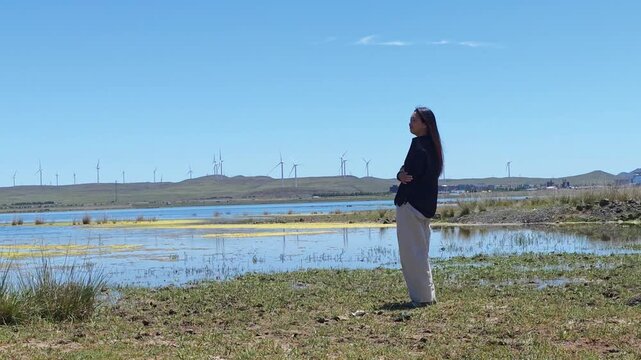 One Asian woman enjoying scenic landscape of salt lake wetland and distant wind turbines in summer in Ulan Hada Volcano Geopark, Ulanqab, Inner Mongolia, China