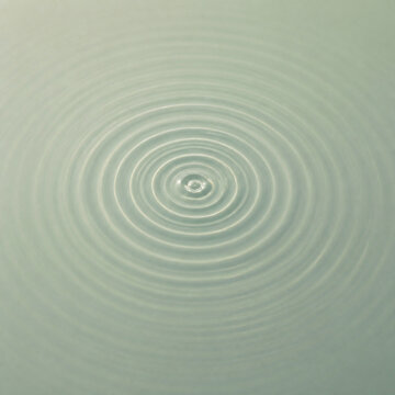 Photorealistic business concept showing concentric ripple rings expanding outward from a single point on a still water surface, overhead, soft even light. Visual metaphor for growth and decisions.