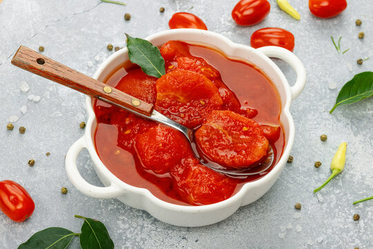 Canned whole peeled tomatoes in tomato juice in a white ceramic bowl with spoon. Rustic food styling