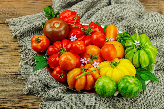Assorted homegrown heirloom tomatoes of various shapes, sizes and colors with small flowers