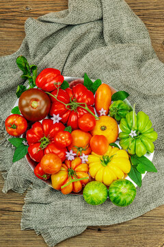 Assorted homegrown heirloom tomatoes of various shapes, sizes and colors with small flowers