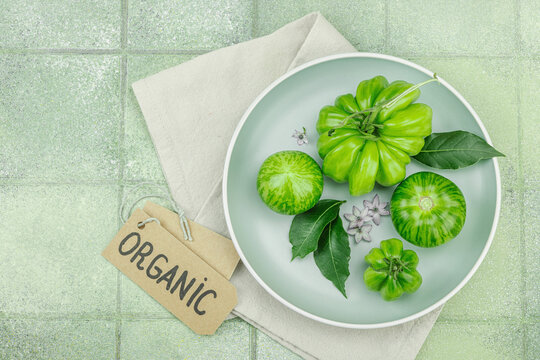 Assorted green heirloom tomatoes with leaves and small flowers on a pale plate with a linen napkin