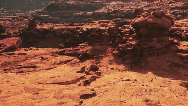 A wide view of a dry desert landscape filled with large rock formations. The ground is rocky and sandy, creating a rough terrain. The scene shows browns and reds and is likely in a warm location.