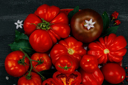 Assorted red homegrown heirloom tomatoes with a cross-section slice, small flowers, salt crystals