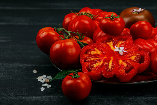 Assorted red homegrown heirloom tomatoes with a cross-section slice, small flowers, salt crystals