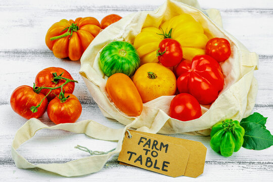 Assorted homegrown heirloom tomatoes in a cotton reusable tote bag with a Farm to Table paper tag