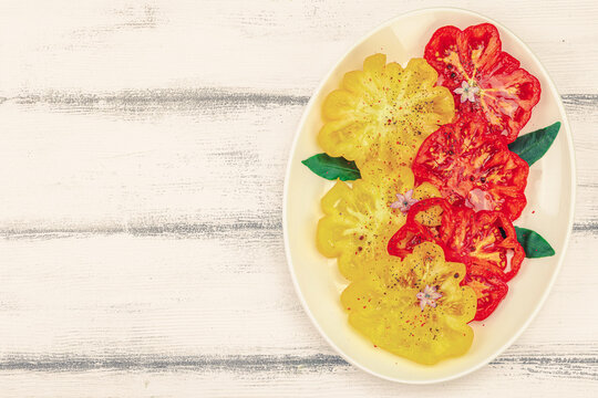 Carpaccio, assorted slices of red and yellow heirloom beefsteak tomatoes seasoned, spices, olive oil