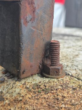 Close-up of rusted bolt and screw welded to an old iron structure on weathered concrete