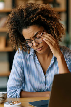 Woman with glasses rubbing her eyes from screen fatigue while working on laptop