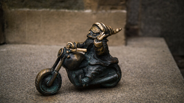 WROCLAW, POLAND  AUGUST 2026 Bronze sculpture of the Wroclaw Gnome named Wentyl riding a motorcycle on a paved street. 