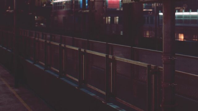A quiet train station at night shows an empty platform with few lights. Nearby, a small structure has knobs and fixtures. The atmosphere indicates a time of waiting.